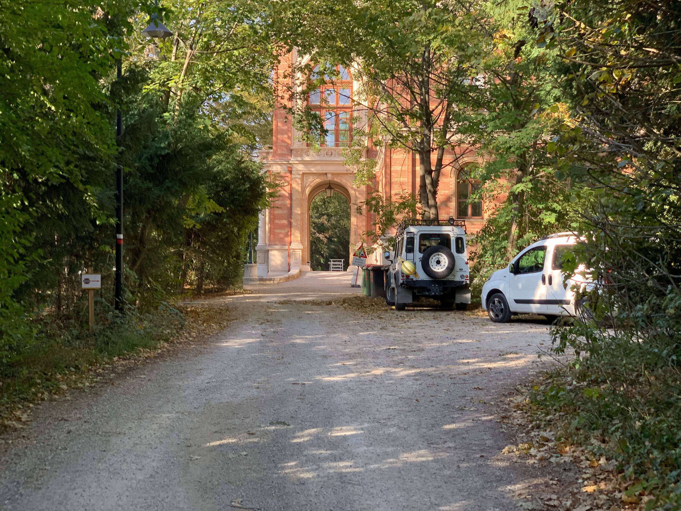 Zwei Autos stehen vor einem backsteinrotem Gebäude, im Hintergrund sind Bäume zu sehen