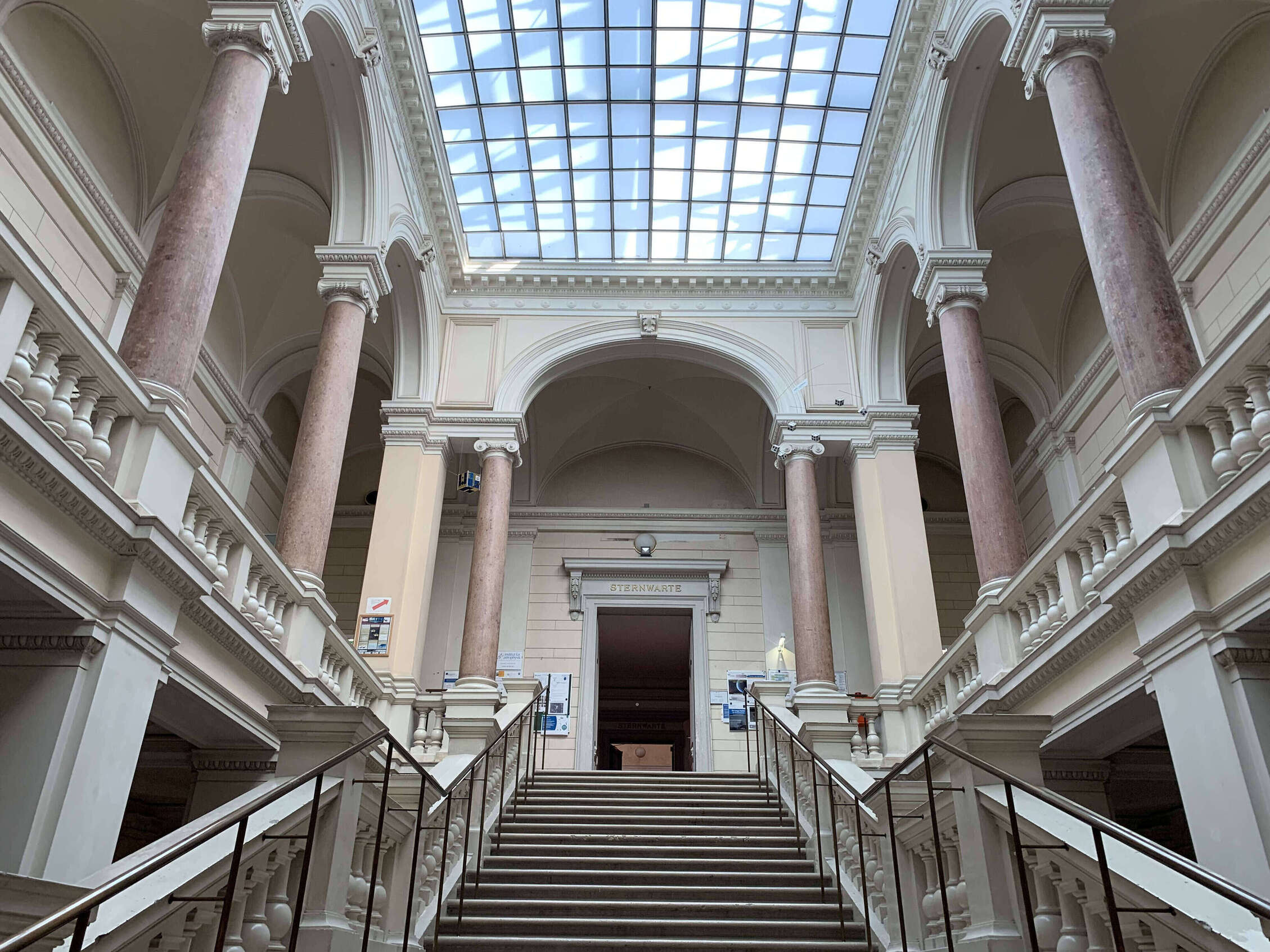 Prächtige Stiegen mit Säulen Galerie führen in das erste Obergeschoss, über dem ganzen eine blaue Glasdecke